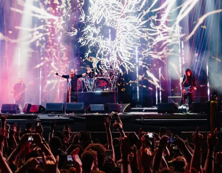 Banda Korn se apresentando ao vivo em um show com luzes e efeitos visuais intensos no palco, diante de uma plateia animada.
