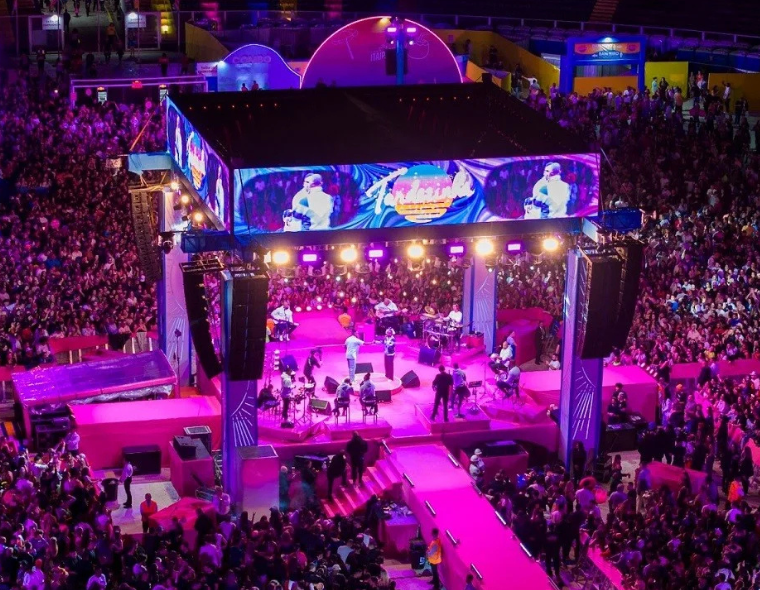 Show do Tardezinha com palco iluminado em tons de rosa e púrpura, multidão de fãs ao redor, e tela de LED exibindo o nome do evento.