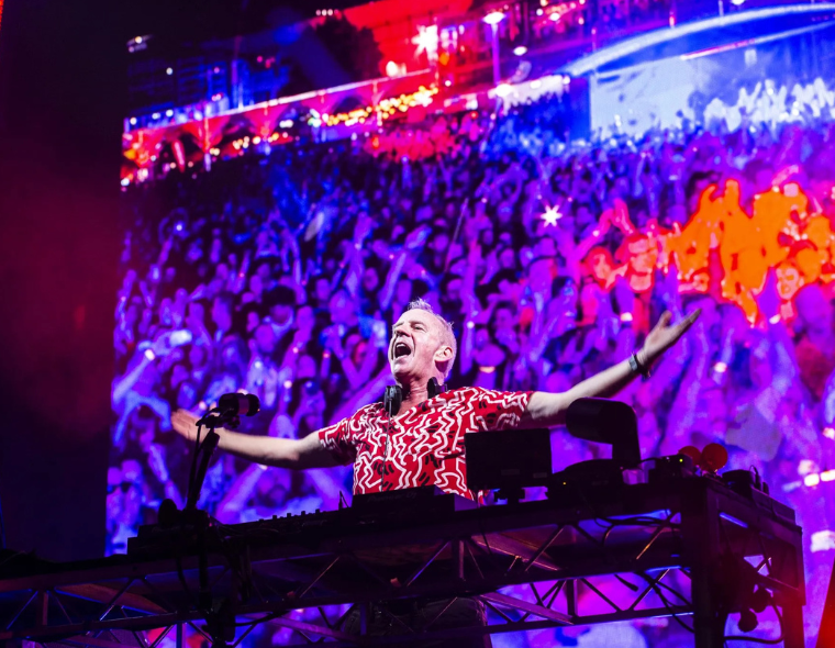 Fatboy Slim no Rock in Rio 2026, animando a multidão no palco New Dance Order com luzes coloridas e grande público ao fundo.